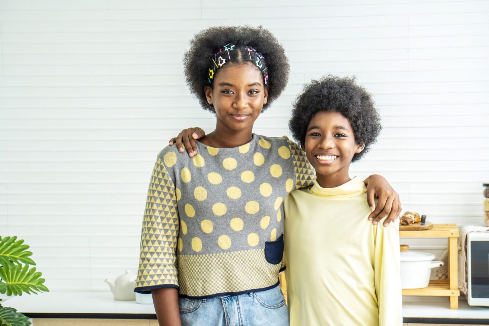 Two young people posing for a picture in front of a wall.