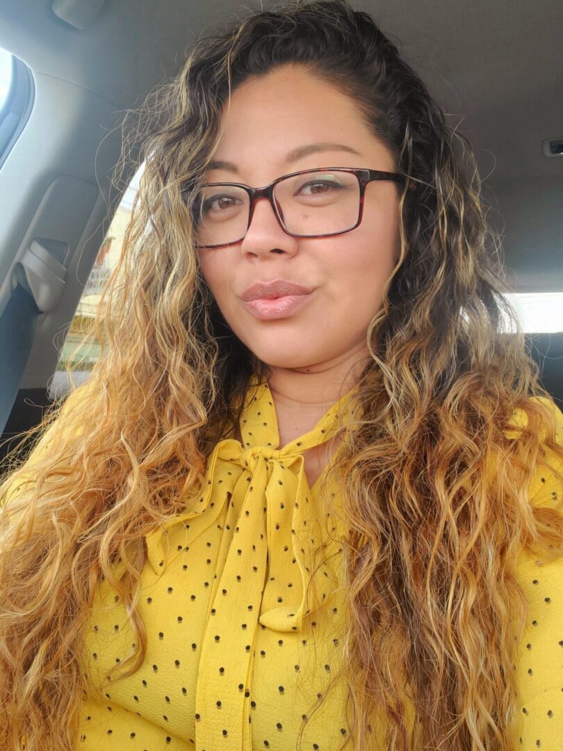 A woman with long hair and glasses in a yellow shirt.