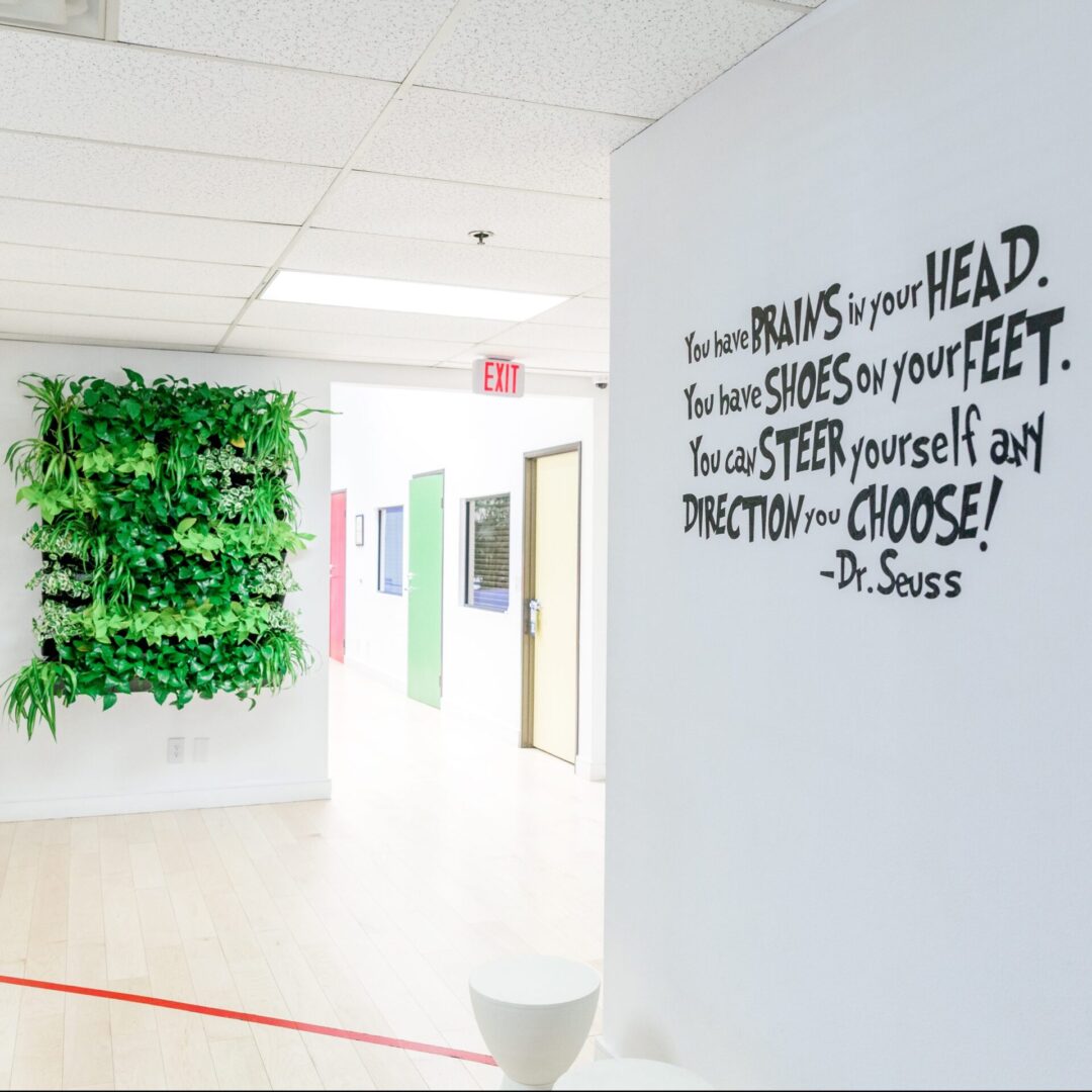 A hallway with a wall of plants and a red toilet.